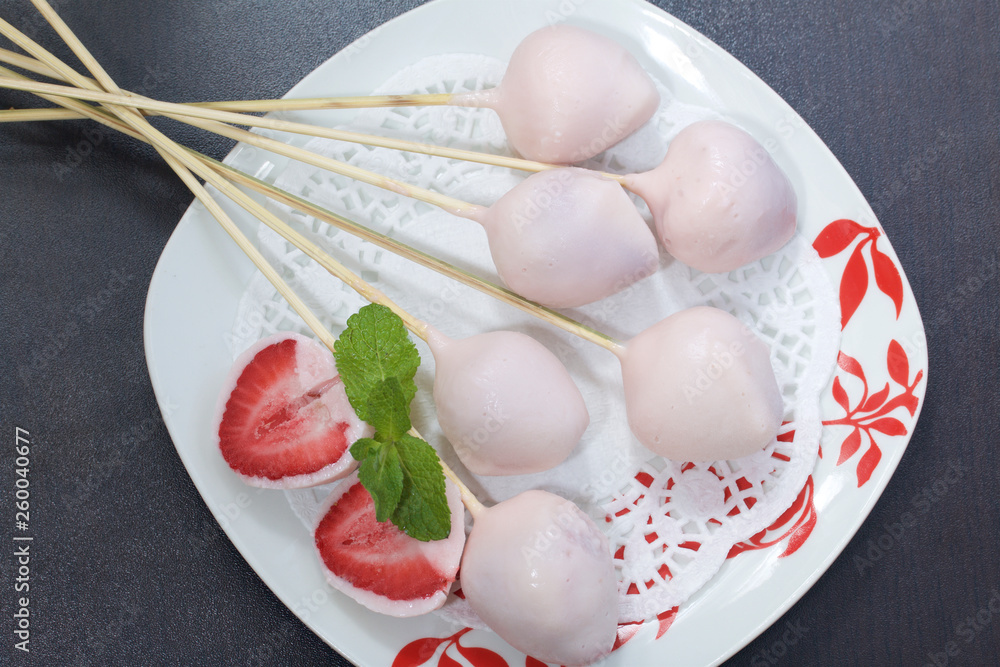 Strawberries in yogurt. Berries are dressed on wooden skewers and dipped in yogurt. Nearby are two halves of dessert. Visible red juicy strawberry flesh. Decorated with mint leaves. Strawberries in yogurt. Berries are dressed on wooden skewers and dipped in yogurt. Nearby are two halves of dessert. Visible red juicy strawberry flesh. Decorated with mint leaves.