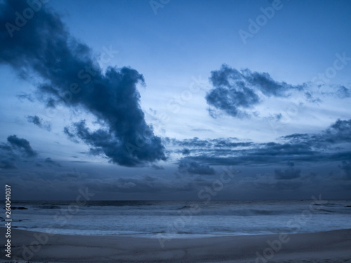Fototapeta Naklejka Na Ścianę i Meble -  Dark moody clouds over ocean at dusk on beach