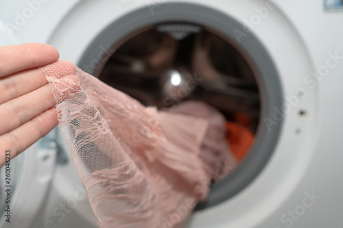 Female hand holding a pink lace dress just washed in an automatic washing machine, delicate wash mode 