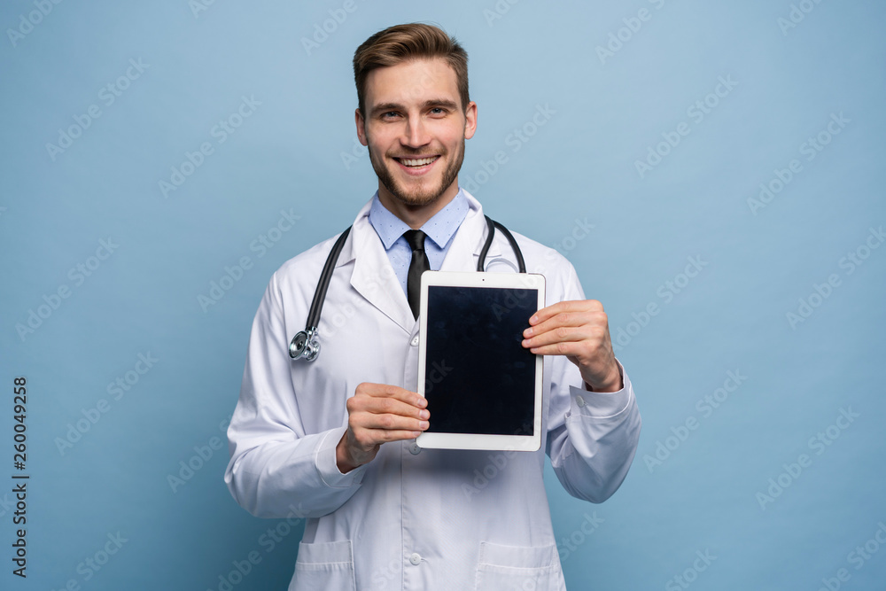 Portrait of friendly doctor presenting empty digital tablet screen. Isolated on light blue. Portrait of friendly doctor presenting empty digital tablet screen. Isolated on light blue.