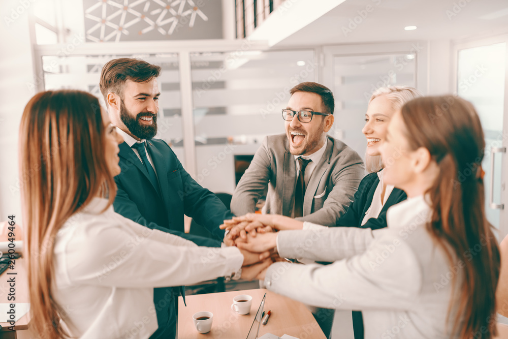 Fototapeta premium Group of cheerful corporate businesspeople in formal wear stacking hands at meeting in boardroom. Catch your people doing something right and let them know you appreciate it.