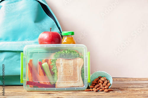 School lunch box with sandwich, vegetables, juice and almonds on table. photo