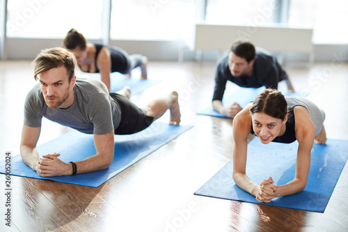 Concentrated motivated young people in sportswear doing elbow plank while strengthening arms and spine at group fitness class photo
