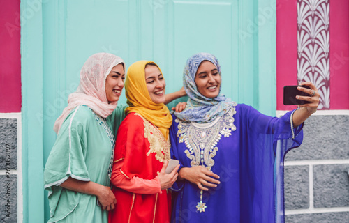 Happy Muslim girls taking selfie with mobile smartphone camera outdoor - Arabian young women making photo for social media network - Friendship, technology, religion and youth people lifestyle concept