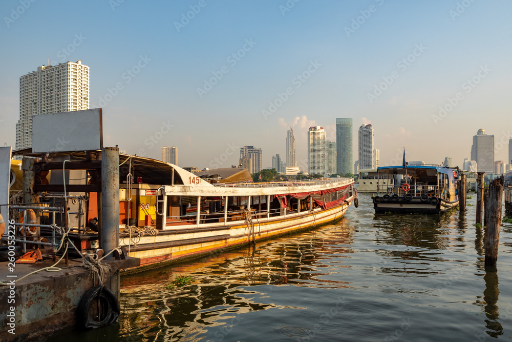 The shuttle boat with morning sun shines, waiting for passengers at the pier with city view and clear blue sky background