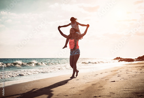 Mother and daughter running together along the seashore on the beach - Happy family piggyback at sunset - Parenthood, childhood, love and happiness concept
