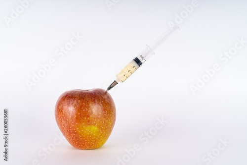Injection of a red apple with a syringe. Antibiotic or GMO. Genetically modified fruit on white background