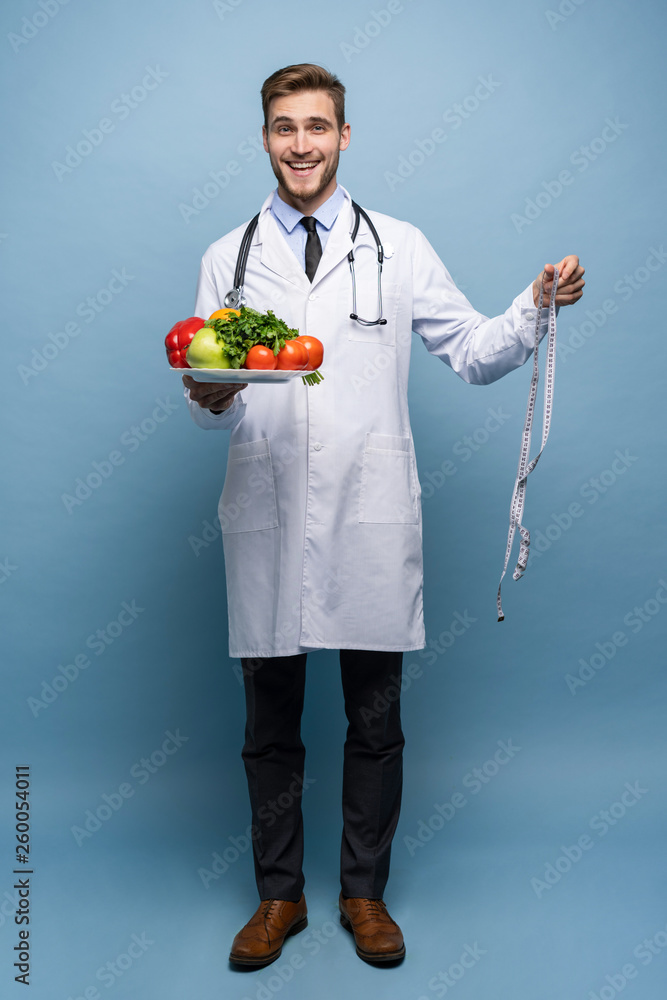Doctor with a measuring tape and a plate with vegetables and fruit isolated on light blue background. Doctor with a measuring tape and a plate with vegetables and fruit isolated on light blue background.