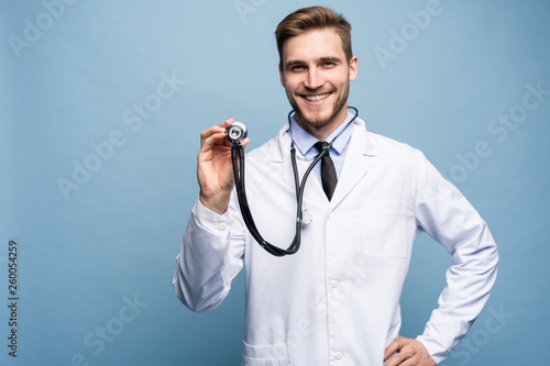 Foto Handsome young medic holding a stethoscope, isolated over light blue