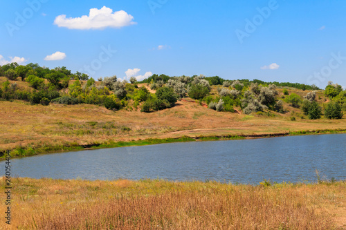 Summer landscape with beautiful lake, green meadows, hills, trees and blue sky