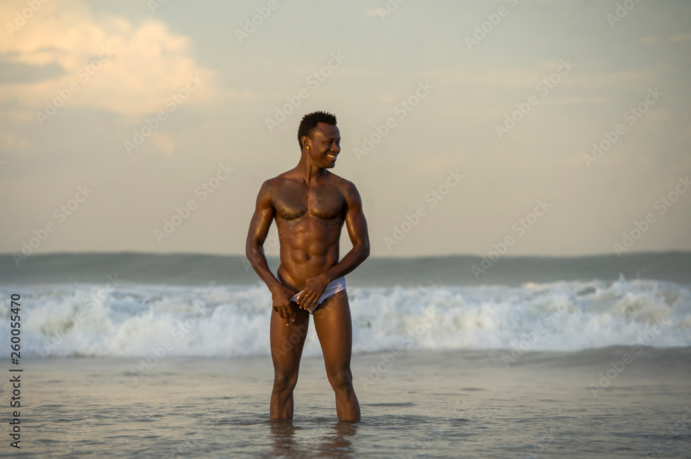 beach portrait of young fit and attractive black afro American man with muscular beautiful body enjoying playful in the sea playing on the water having fun
