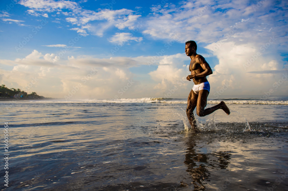 happy and attractive black African American man with fit healthy and muscular body running on beach sea water having fun enjoying Summer holidays feeling free