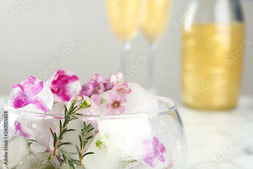 Glass with floral ice cubes on blurred background, closeup. Space for text