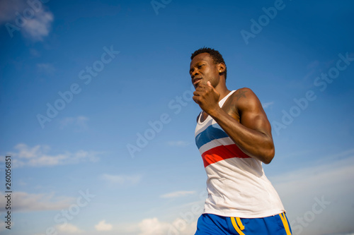 young athletic and attractive black African American runner man doing running workout training on desert beach in fitness and wellness isolated on blue sky