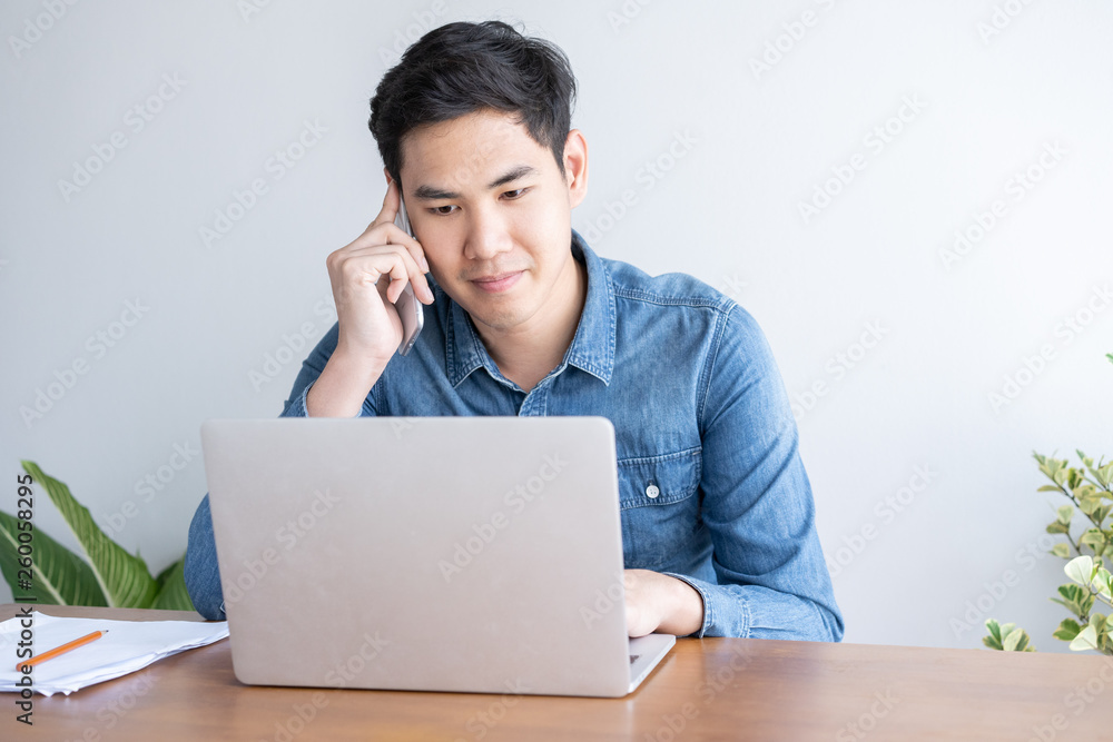 Young asian businessman wear blue shirt talking on a mobile phone and working on his laptop in office Young asian businessman wear blue shirt talking on a mobile phone and working on his laptop in office