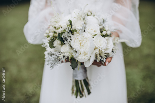 bride in white dress holding a bouquet of white flowers and greenery