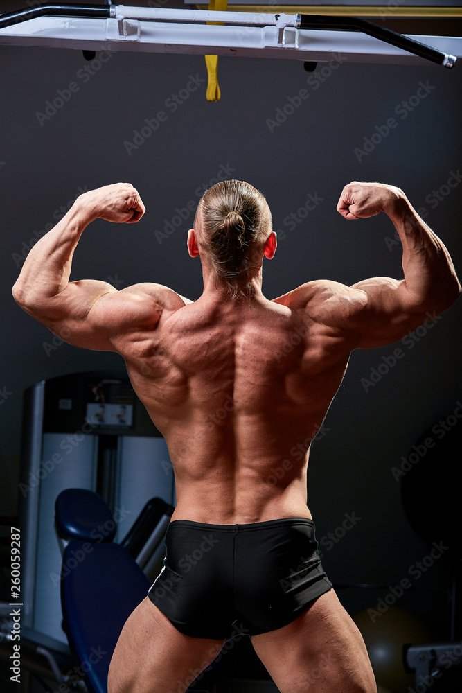 Athletic man posing. Photo of man with perfect physique on black background. Back view. Strength and motivation Athletic man posing. Photo of man with perfect physique on black background. Back view. Strength and motivation