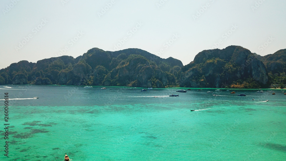 Blue clear water with boats. Green tropical island Phi Phi, palm trees grow. Shooting from a drone from the air. Beautiful seascape. Turquoise color of the water, you can see the bottom and corals. Blue clear water with boats. Green tropical island Phi Phi, palm trees grow. Shooting from a drone from the air. Beautiful seascape. Turquoise color of the water, you can see the bottom and corals.