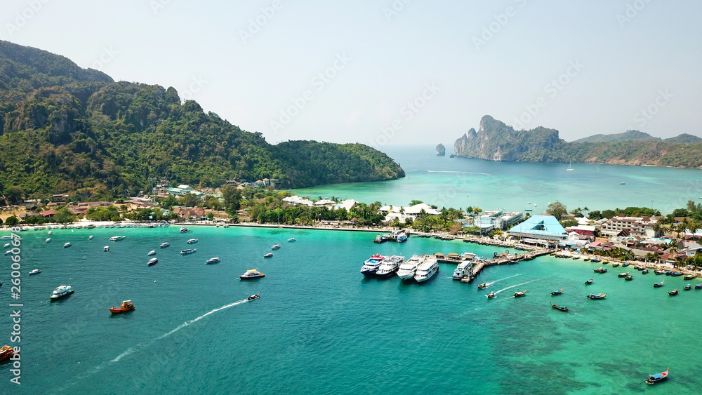 Blue lagoon. Bay with clear sea. Green island with palm trees, Paradise. Drone footage. White sand on the beach. Lots of boats. You can see the ocean floor and sky. Travel in Asia, Phi, Thailand.
