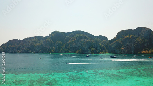 Blue clear water with boats. Green tropical island Phi Phi, palm trees grow. Shooting from a drone from the air. Beautiful seascape. Turquoise color of the water, you can see the bottom and corals.