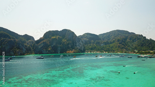 Blue clear water with boats. Green tropical island Phi Phi, palm trees grow. Shooting from a drone from the air. Beautiful seascape. Turquoise color of the water, you can see the bottom and corals. © SergeyPanikhin