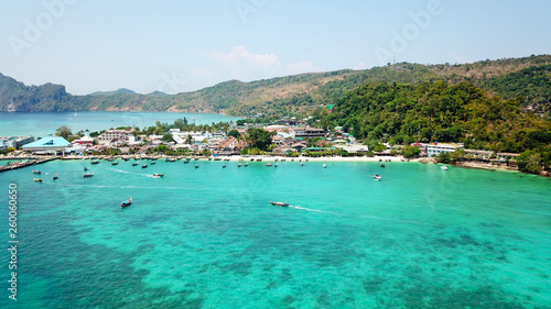 Fototapeta Naklejka Na Ścianę i Meble -  Blue lagoon. Bay with clear sea. Green island with palm trees, Paradise. Drone footage. White sand on the beach. Lots of boats. You can see the ocean floor and sky. Travel in Asia, Phi, Thailand.
