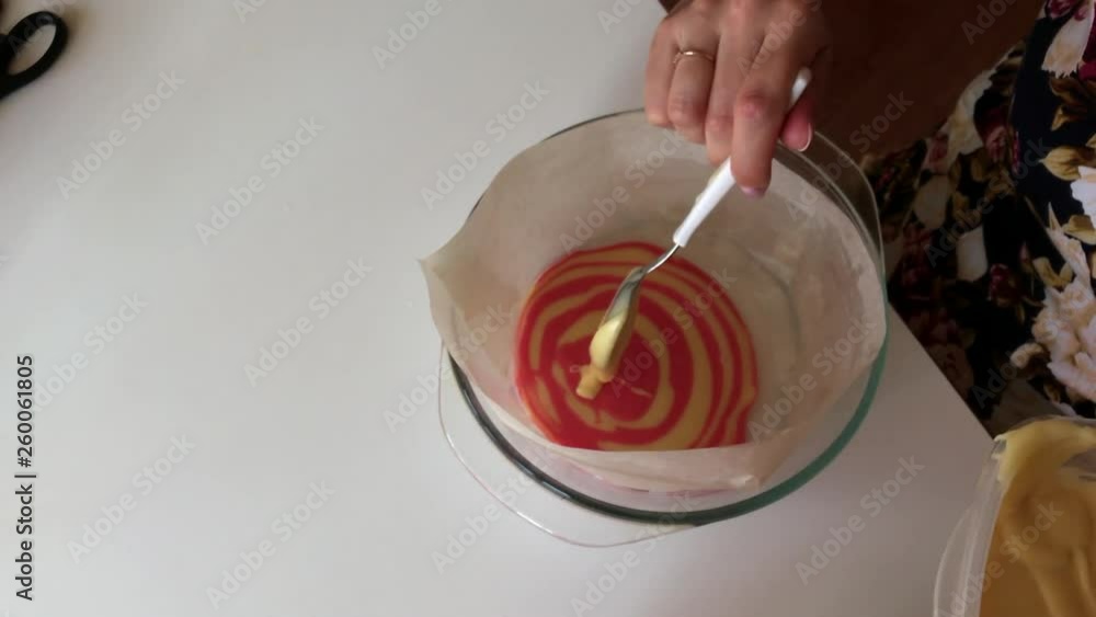 A woman puts a spoon of dough of different colors in a glass baking dish. To make a cake. A woman puts a spoon of dough of different colors in a glass baking dish. To make a cake.