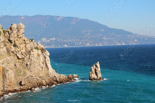 The rocky Black Sea coast of the Crimean peninsula near the town of Gaspra, part of Big Yalta. Above the blue water of a picturesque bay rises a cliff with a small statue of an eagle.