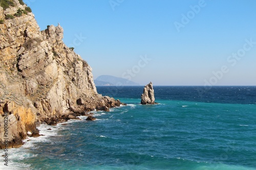 The rocky Black Sea coast of the Crimean peninsula near the town of Gaspra, part of Big Yalta. Above the blue water of a picturesque bay rises a cliff with a small statue of an eagle.