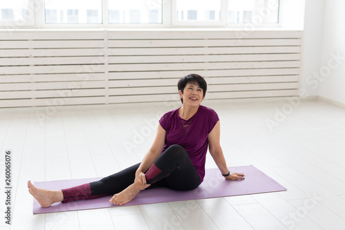 People, sport, yoga and healthcare concept - Smiling middle-aged woman sitting on exercise mat