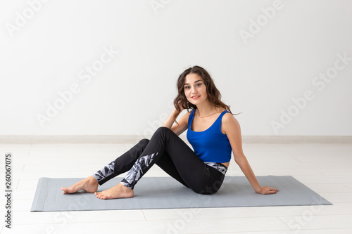 People, sport, yoga and healthcare concept - Smiling young woman sitting on exercise mat