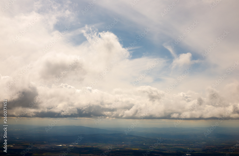 Obraz premium clouds at a level with view down to earth at fields and hills