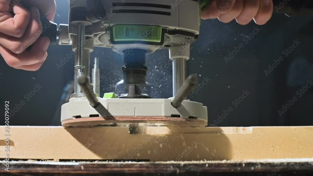 Close-up of a carpenter's hand working with an manual electric cutter in a home workshop. Finishing wooden parts in slow motion Close-up of a carpenter's hand working with an manual electric cutter in a home workshop. Finishing wooden parts in slow motion