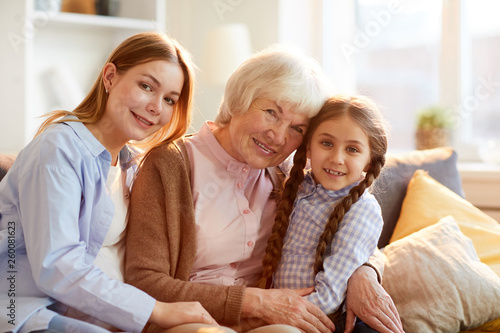 Three generations of women, girl, mother and grandmother posing for family portrait in warm sunlight, all looking at camera
