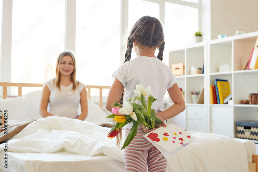 Back view portrait of cute little girl hiding bouquet surprising mother on Birthday, copy space