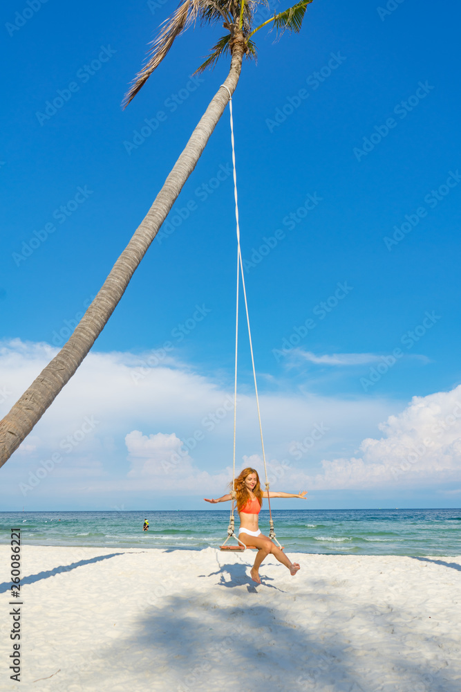 Red haired girl in bikini swinging on the paln on beautiful beach with white sand and crystal water in Phu quoc island Vietnam ,travel concept