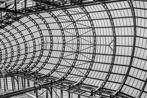 Through the glass covered steel roof, a black and white look up at a London shopping gallery area.