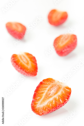 Red fresh strawberries cut into half arranged on a white background