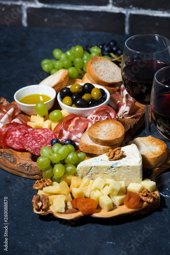 cheese platter, bread, fruit and cold cuts to wine on dark background, vertical
