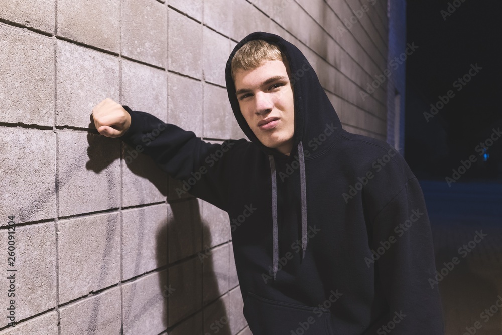 Hooded teenager leaning against a brick wall in an alleyway. He is suffering from depression. Hooded teenager leaning against a brick wall in an alleyway. He is suffering from depression.