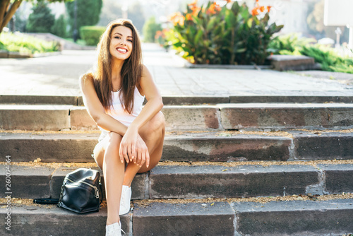 Pretty young smiling brunette girl relaxing outdoor on the street.