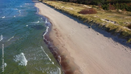 Drone shot of the Beach of Preila, Curonian Spit, Lithuania, with waves crashing on the shore and forests over the beach, on a sunny day with clouds photo