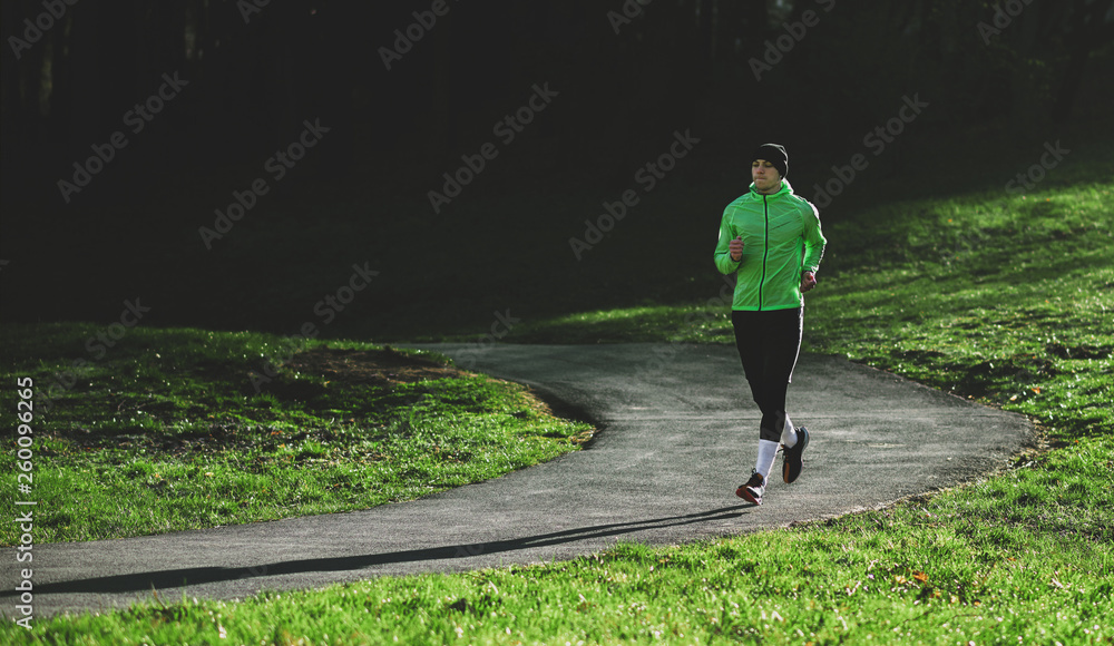 Fototapeta premium Horizontal outdoor shot of an athlete young man running on a trail. Athletic male jogging in the park in the morning in a sunny day. People, healthy lifestyle and sport concept