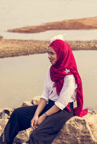  Women muslim, women islamic,wearing a red fabric head covering adorn with white fabric flowers wear shirt white sit on the rock poses photography  before to ramadan month.
