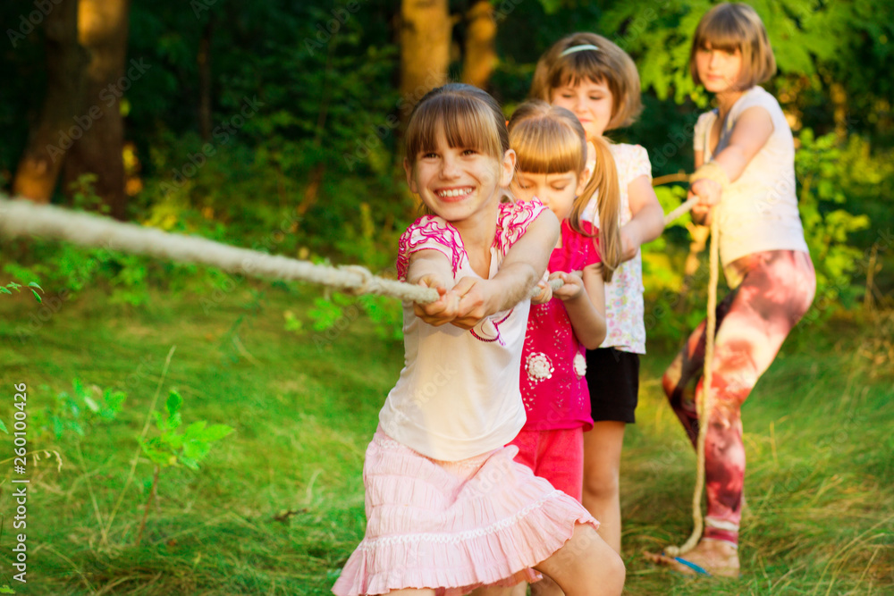 Group of happy children playing tug of war outside on grass. Kids pulling rope at park. Group of happy children playing tug of war outside on grass. Kids pulling rope at park.