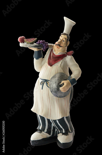 Decorative toy chef with a spacing in his hands. Souvenir. Isolated on black background.