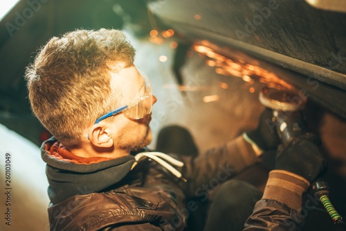 man in goggles for cutting metal  stpli with an electric rotating angle grinder and works by generating metallic sparks. construction industry  