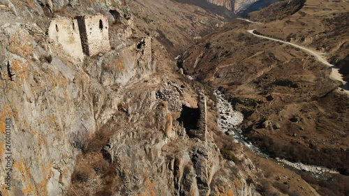 The ruins of ancient towers on a rock in the mountains of Upper Balkaria. Aerial view of the gorge with a dirt road and a mountain river in the mountains of the Caucasus. sunny day photo