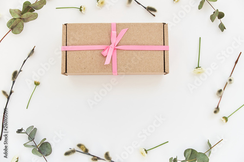 Spring composition with a gift box with a pink bow and green sprigs and flowers lying on a white background. Background, copy space for text, top view, close-up © Stas