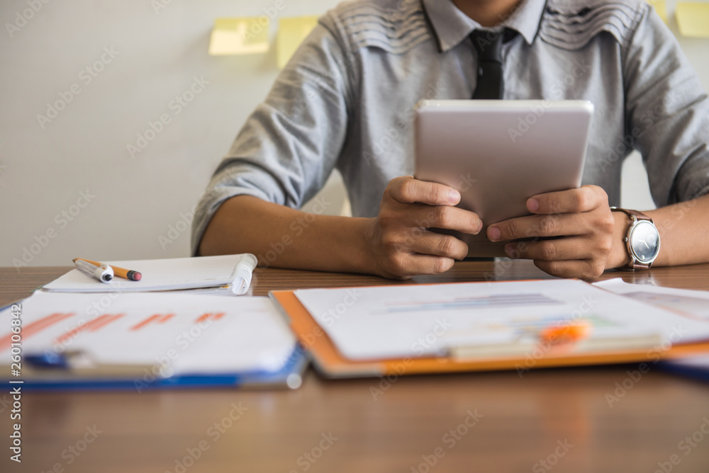 Young man using tablet with financial report on desk Young man using tablet with financial report on desk